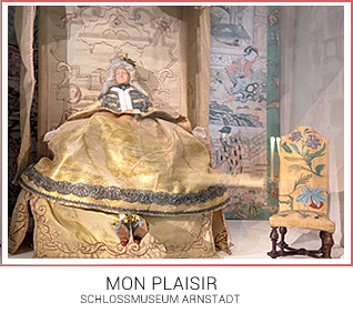 Kleine Wachspuppe in einem Tronsessel